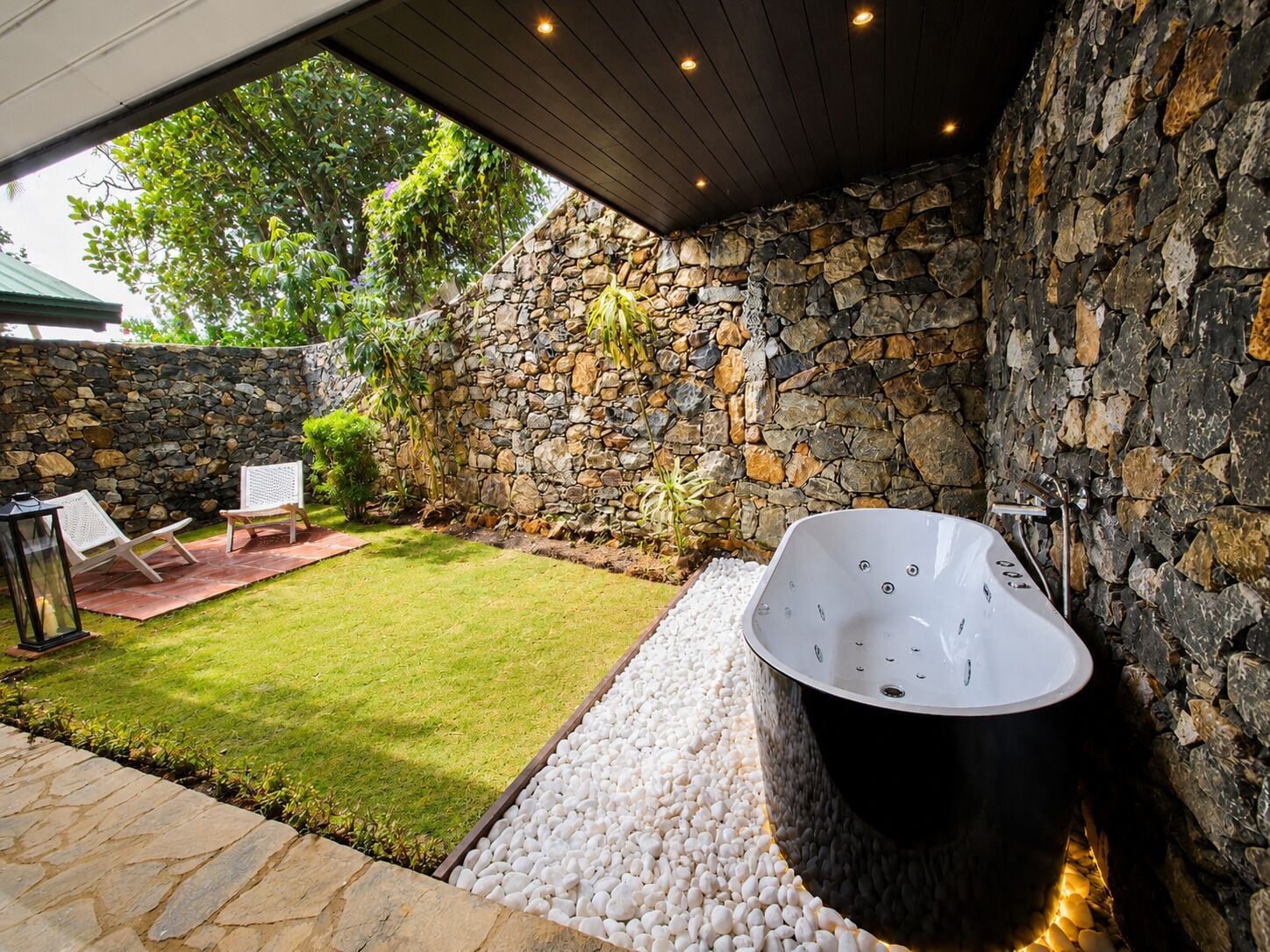 A spa area with a stone wall, a hot tub, and a small lawn with chairs.
