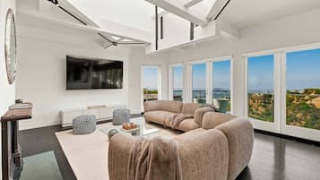 Una sala moderna con un amplio sofá modular, un televisor de pantalla plana y vistas de la ciudad a través de grandes ventanales.