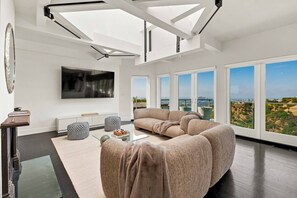 A modern living room with a large sectional sofa, a flat-screen TV, and a view of the city through large windows.
