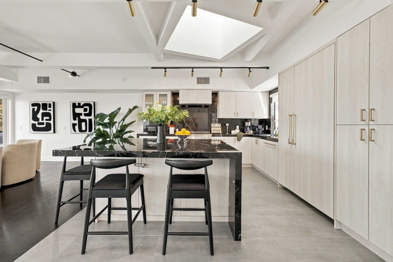 A modern kitchen with a central island, bar stools, and a ceiling skylight.
