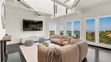 A modern living room with a large sectional sofa, a flat-screen TV, and a view of the city through large windows.