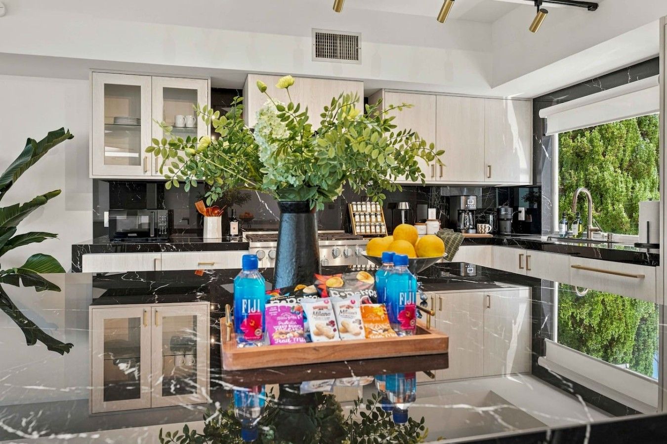 A modern kitchen with a central island, white cabinetry, and a large window providing a view of greenery.