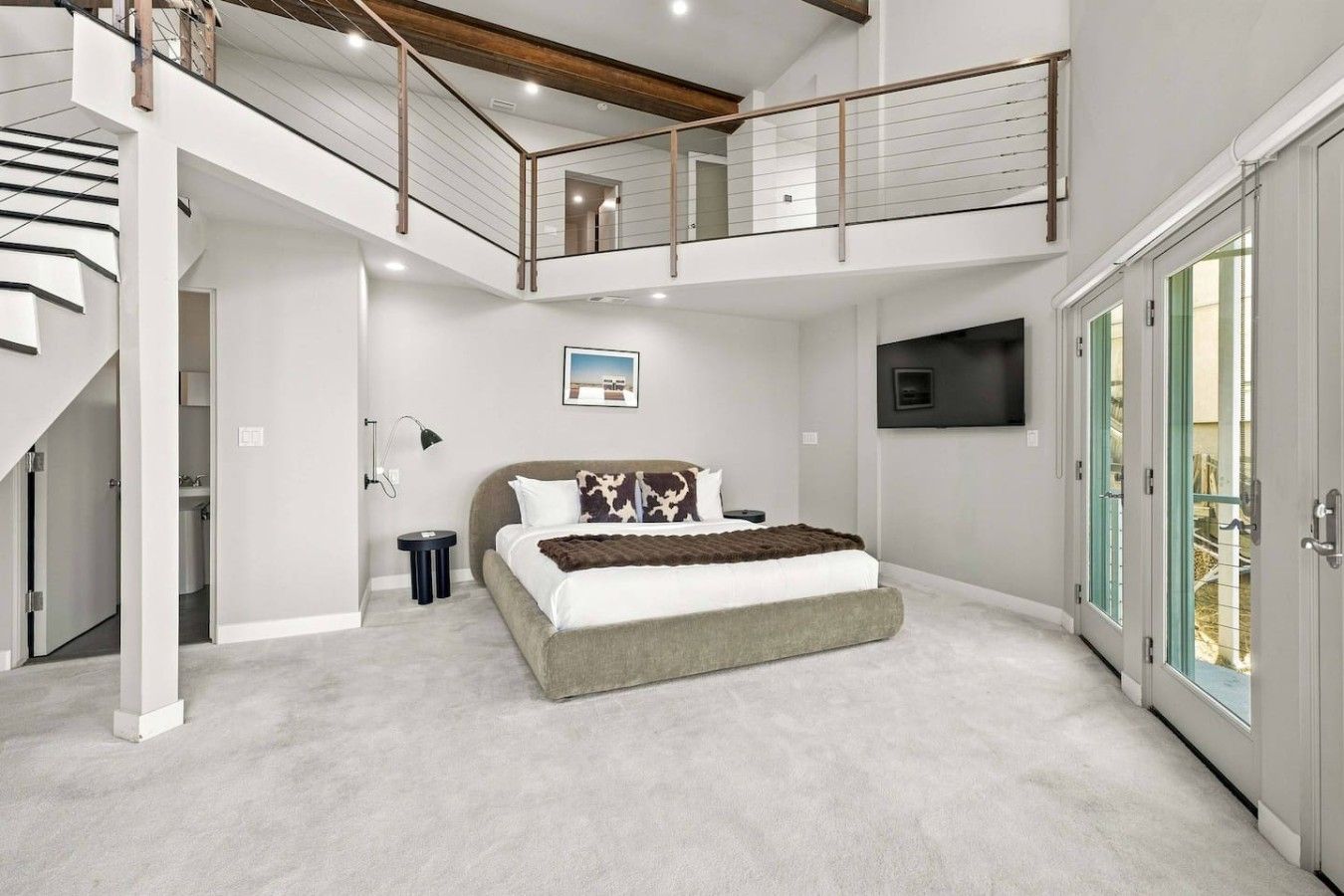 A bedroom with a large bed, a TV mounted on the wall, and a balcony with a railing.