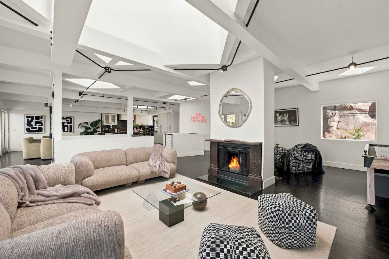 A modern living room with a fireplace, a sofa, a coffee table, and a checkered ottoman.