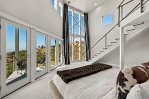 A bedroom with a large bed, a view through the window, a staircase, and a balcony.