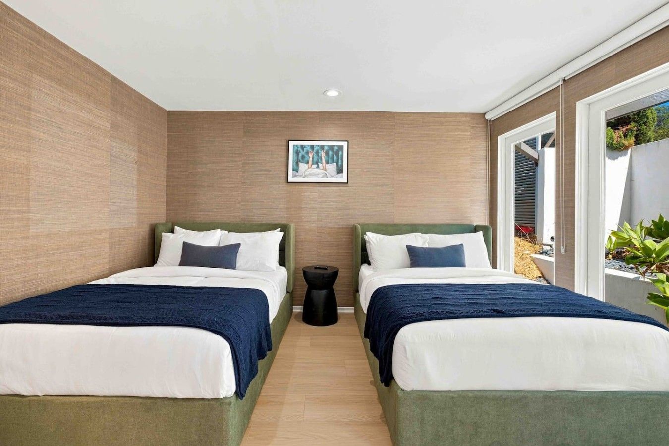 Habitación de hotel con dos camas, una mesita auxiliar y un cuadro en la pared.