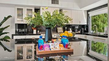 A modern kitchen with a central island, white cabinetry, and a large window providing a view of greenery.