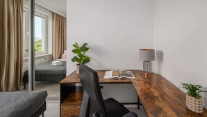 A modern hotel room with a wooden desk, a chair, a bed, a window with curtains, a plant, and a lamp. - Flat With Quiet Courtyard (Warsaw)