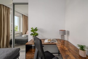 Ein modernes Hotelzimmer mit einem Holztisch, einem Stuhl, einem Bett, einem Fenster mit Vorhängen, einer Pflanze und einer Lampe.