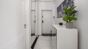 A hallway with a white door, a glass door, a potted plant, and a cityscape painting on the wall. - Flat With Quiet Courtyard (Warsaw)