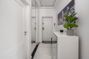 Ein Korridor mit einer weißen Tür, einer Glastür, einem Blumentopf und einem Stadtbild an der Wand.