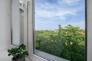 A window with a view of a tree-lined street and buildings. - Flat With Quiet Courtyard (Warsaw)