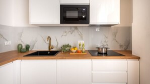 A kitchen with white cabinets, a black microwave, a sink, and a wooden countertop. - GuestHost - Casa Tramonto Elegant Flat (Palermo)