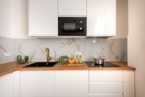 A kitchen with white cabinets, a black microwave, a sink, and a wooden countertop. - GuestHost - Casa Tramonto Elegant Flat (Palermo)