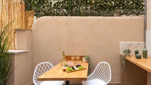 A dining area with a wooden table, two white chairs, a bottle of wine, and a plate of food. - GuestHost - Casa Tramonto Elegant Flat (Palermo)