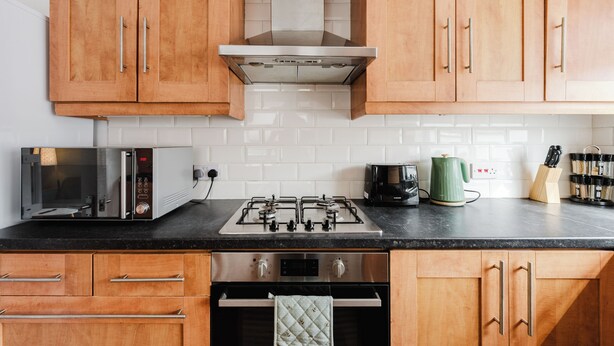 A kitchen with wooden cabinets, a gas stove, a built-in oven, and a microwave. - 4 bed, 4 en-suite house (Warrington)