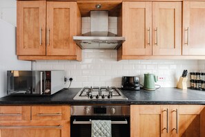 Une cuisine avec des meubles de rangement en bois, une cuisinière à gaz, un four encastré et un four à micro-ondes.
