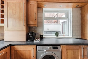 A compact kitchen with wooden cabinets, a built-in washing machine, and a window with a view of a brick building. - 4 bed, 4 en-suite house (Warrington)