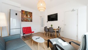 A modern living room with a sofa, a red chair, a dining table with chairs, a TV mounted on the wall, and a refrigerator. - 4 bed, 4 en-suite house (Warrington)