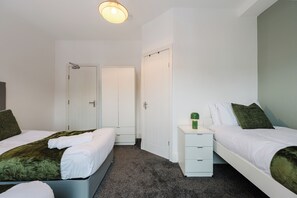 A hotel room with two beds, a small bedside table, a wardrobe, and a ceiling light. - 4 bed, 4 en-suite house (Warrington)