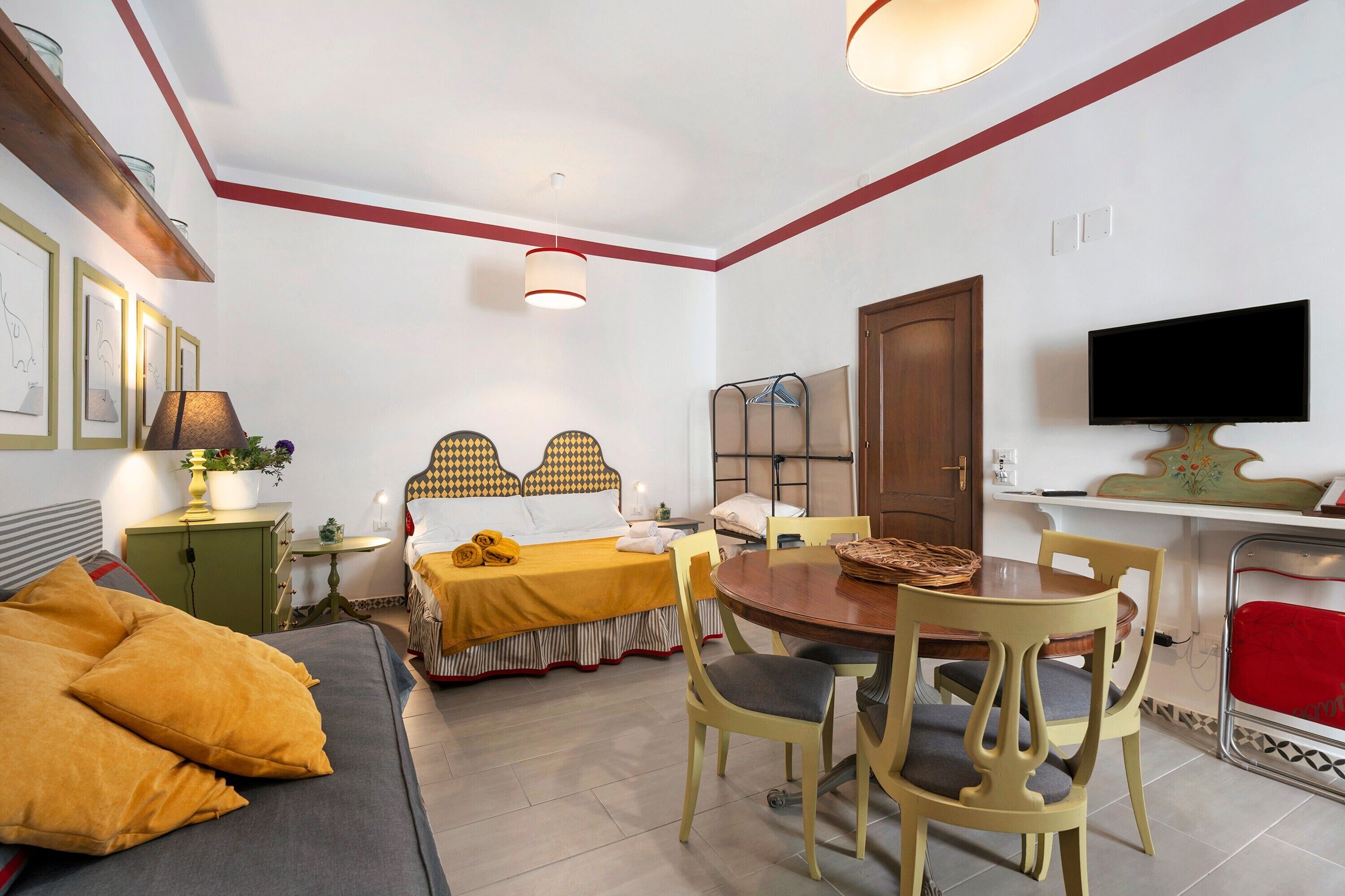 Ein gemütliches Hotelzimmer mit einem Bett, einem Esstisch, Stühlen, einem Fernseher und einem kleinen Tisch mit einer Lampe.