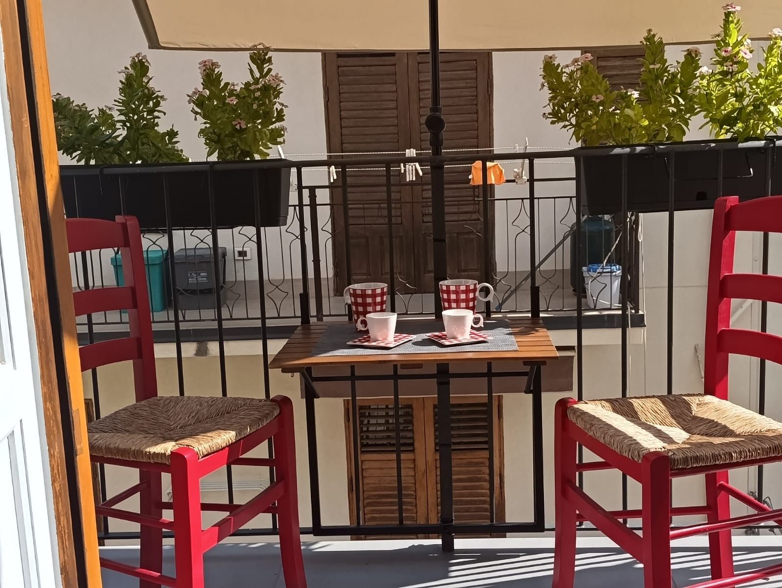 Ein Balkon mit zwei roten Stühlen, einem Tisch und zwei weißen Tassen mit roten Mustern.