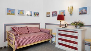 Un dormitorio con un sofá a cuadros, una mesita de noche con una lámpara y un aparador con cajones.