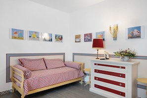 Une chambre avec un canapé à carreaux, une table de chevet avec une lampe et une commode avec des tiroirs.