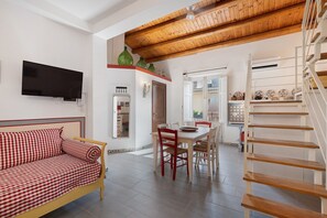 A living room with a sofa, a dining area with a table and chairs, a kitchen with a stove, and a staircase. - Apartment 'Duchessa' with Balcony, Wi-Fi and Air Conditioning (Castellammare del Golfo)