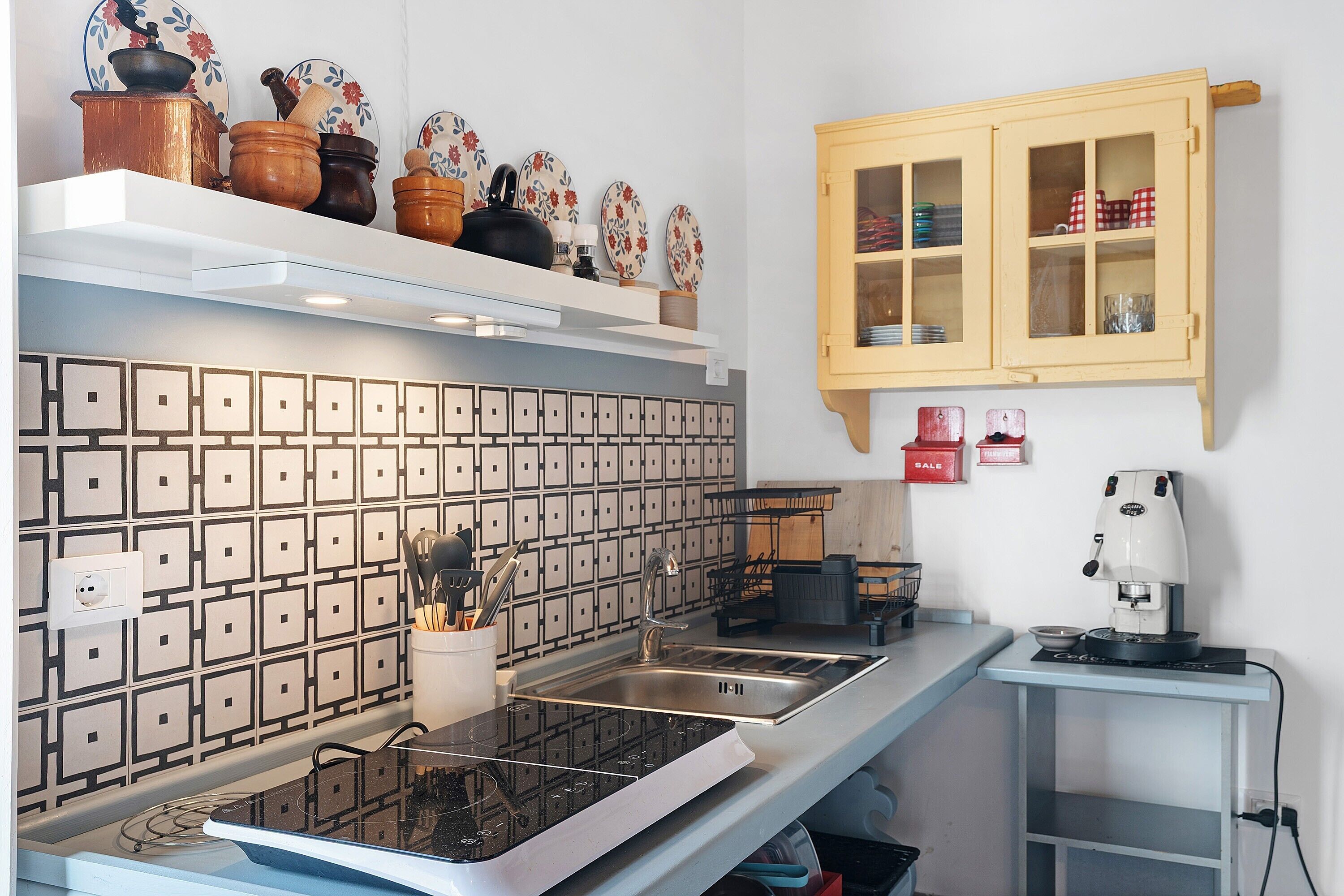 Eine Küche mit modernem Herd, einer Kaffeemaschine und einem Schrank mit Glastüren.