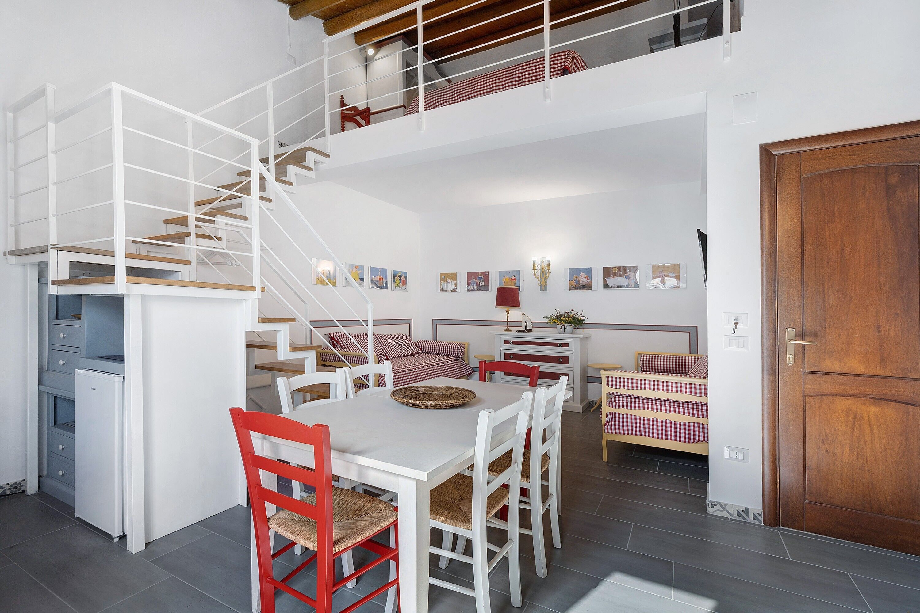 A spacious kitchen with a dining area, a staircase, and a bedroom with a wooden door.