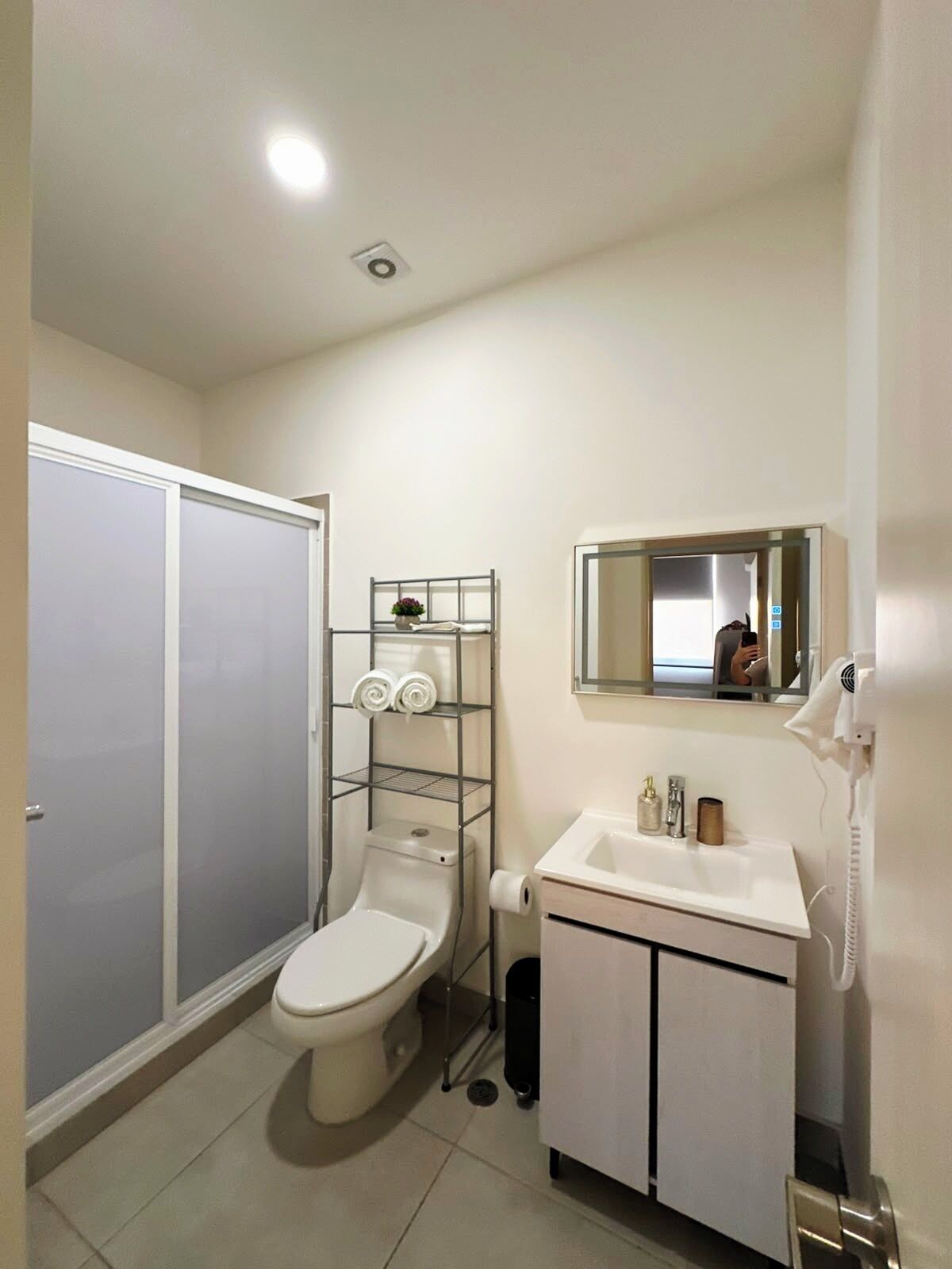 A bathroom with a toilet, a shelf with towels, a mirror, and a sink.