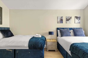 A hotel room with two beds, a nightstand, a lamp, and three wall-mounted artworks. - Steps To The Shard, City & Riverside | Modern Flat (Greater London)
