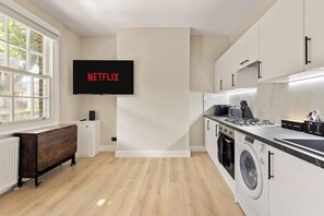 A modern kitchen with a built-in washer and dryer, a wooden cabinet, and a wall-mounted television displaying 'NETFLIX'. - Steps To The Shard, City & Riverside | Modern Flat (Greater London)
