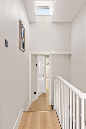 A hallway with a skylight, white walls, and a wooden floor. - Steps To The Shard, City & Riverside | Modern Flat (Greater London)