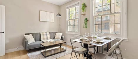 A modern living room with a grey sofa, a coffee table, and a dining table set for four.