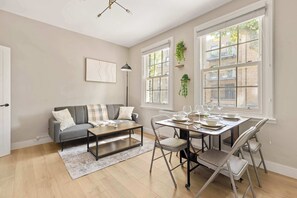 A modern living room with a grey sofa, a coffee table, and a dining table set for four. - Steps To The Shard, City & Riverside | Modern Flat (Greater London)