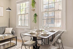 A dining area with a table set for six, chairs, and a window with a view of buildings. - Steps To The Shard, City & Riverside | Modern Flat (Greater London)