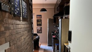 Un pasillo estrecho con un muro de madera en un lado y una zona de cocina en el otro, que incluye un refrigerador, un fregadero y una encimera.