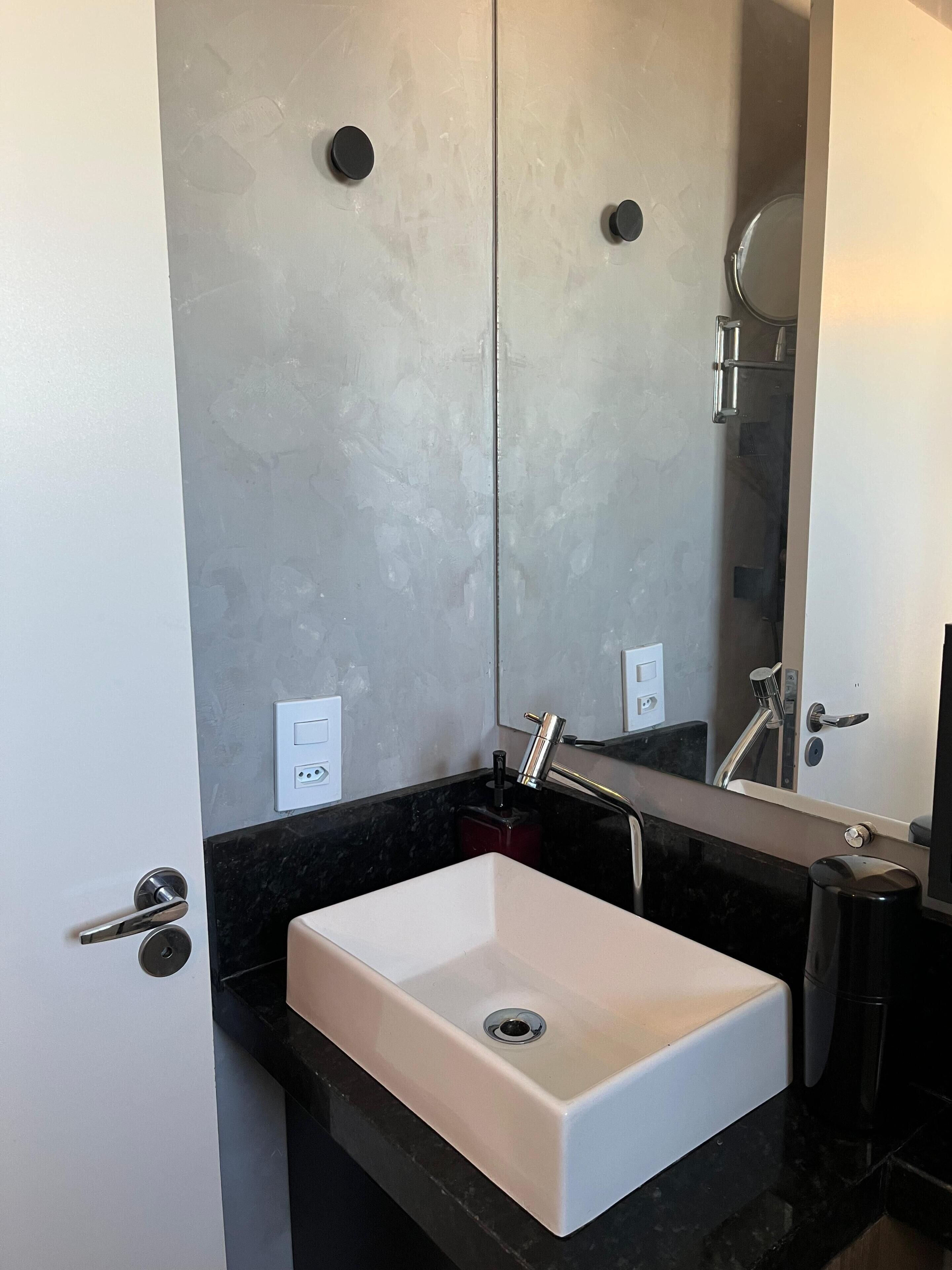 A bathroom with a white sink, black countertop, and a large mirror.