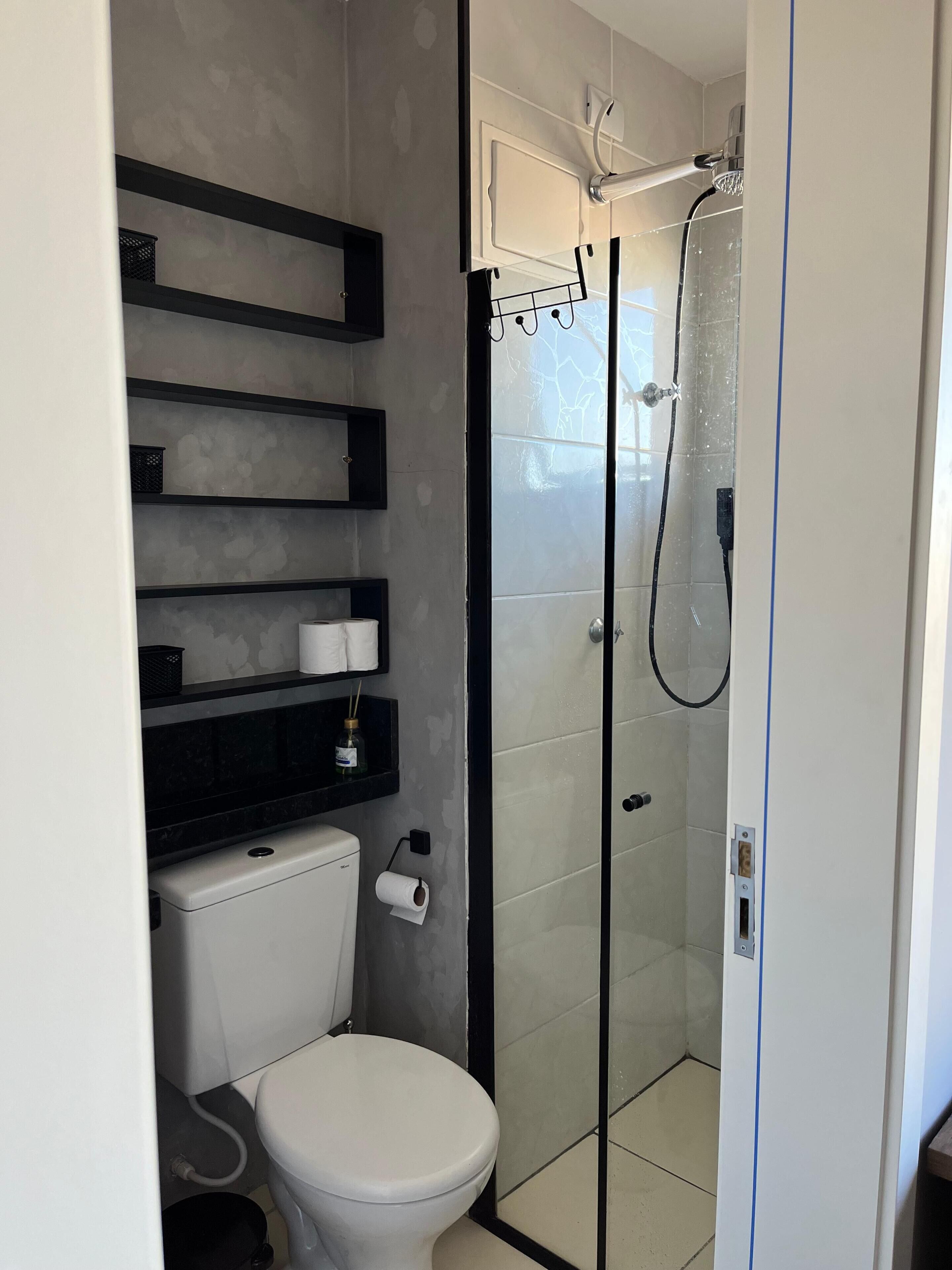 Uma casa de banho moderna com sanita, cabine de duche e prateleiras embutidas com artigos de higiene pessoal.