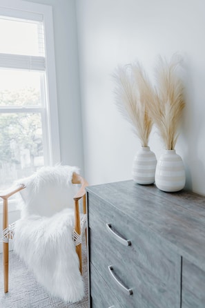 A room with a white chair, a grey cabinet, and two white vases with pampas grass. - 2bdr Townhouse in Franklinton - Fenced in Backyard (Columbus)