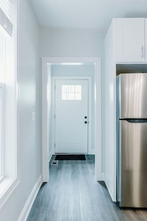 A hallway with a white door, a stainless steel refrigerator, and a light blue wooden floor. - 2bdr Townhouse in Franklinton - Fenced in Backyard (Columbus)