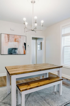 A dining area with a wooden table and benches, a modern chandelier, and abstract wall art. - 2bdr Townhouse in Franklinton - Fenced in Backyard (Columbus)