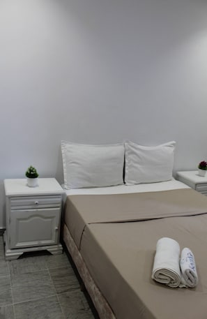 Ein Hotelzimmer mit Bett, Nachttisch, einer kleinen Topfpflanze und einem ordentlich gefalteten Handtuch.