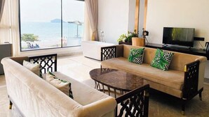 Ein modernes Wohnzimmer mit Sofa, Couchtisch und Fernseher. Ein großes Fenster bietet Blick auf das Meer.
