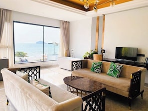 Una sala de estar moderna con un sofá, una mesa de centro y un televisor. Se ve una ventana grande con vistas al mar.