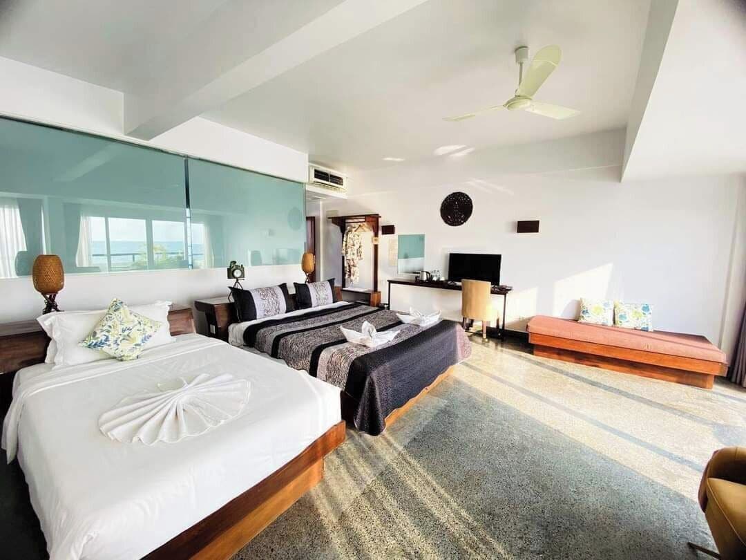 A modern hotel room with two beds, a sofa, a TV, and a ceiling fan.
