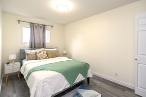 Quarto com cama, mesas de cabeceira, abajur, janela com cortinas e porta.