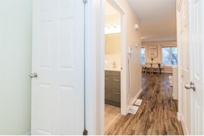 A hallway leading to a kitchen with a dining area, wooden flooring, and white walls. - Bright 3BR Home 4 Min UofM, Shops & Private Parking (Winnipeg)